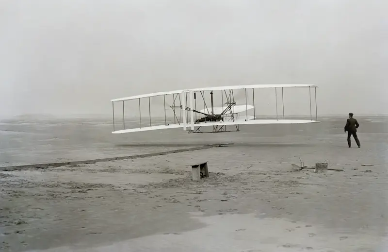 The Wright Flyer lifts off at Kill Devil Hills on December 17, 1903, Orville at the controls and Wilbur running alongside. Photograph by John T. Daniels.