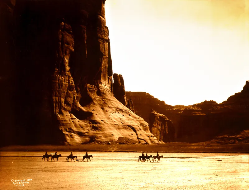 Canyon de Chelly, Diné (Navajo), Edward S. Curtis, 1904. Seven Diné riders cross beneath sheer canyon walls in one of Curtis's most famous images.