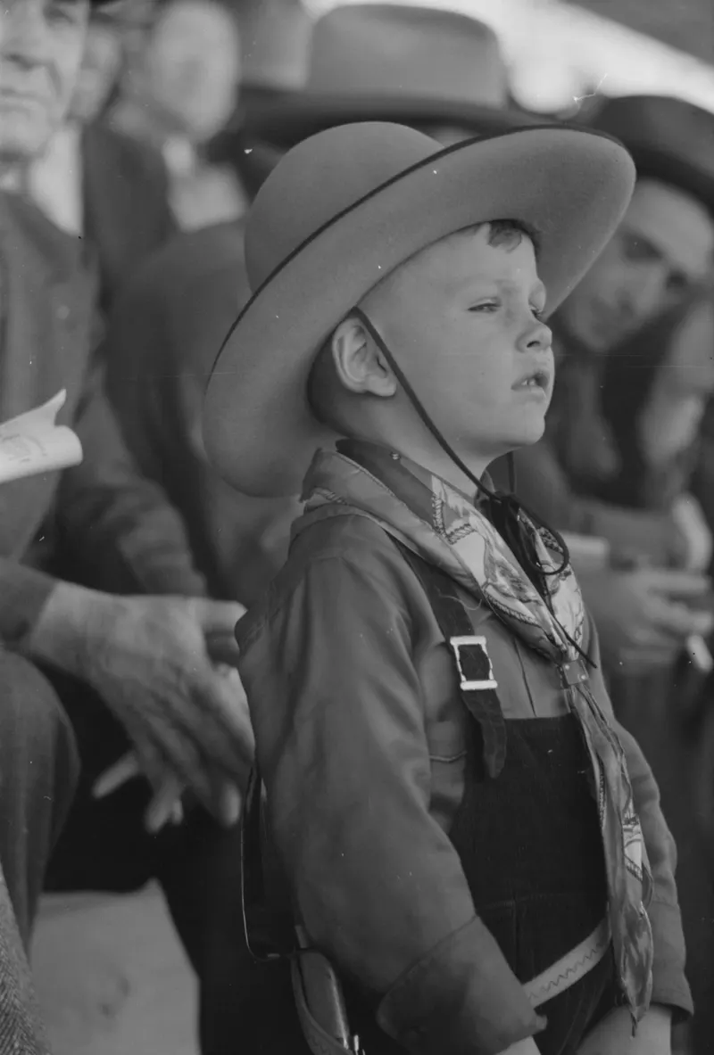 Youngster in Cowboy Costume, 1940 (Russell Lee): A boy in a wide-brimmed cowboy hat and patterned neckerchief watches the rodeo from the crowd